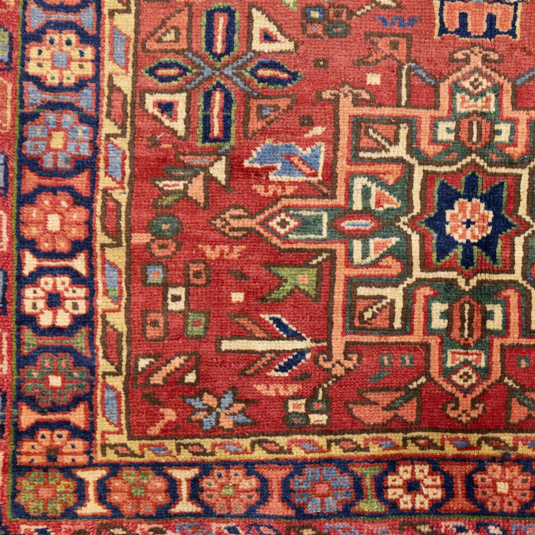 North West Persian Karajeh hand-knotted runner, madder red field, decorated with a vertical sequence of bold geometric medallions, interspersed with stylized floral and tribal motifs, framed by a dark ground border of angular palmettes and rosettes with multiple guard stripes, with cotton fringe ends 