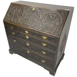 18th century heavily carved oak bureau, the fall front relief carved with three arches enclosing plants and flower head decoration, the interior fitted with pigeonholes, drawers and cupboard, four graduating cock-beaded drawers below, carved with lunettes and trailing foliage decoration, on bracket feet