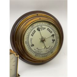 A mid-20th century  hall barometer with a compensated Aneroid movement, sixteen-centimetre silver painted dial measuring barometric air pressure from twenty-six to thirty-one point nine inches, weather predictions and trend written in black upper- and lower-case gothic script and roman capitals with a blue steel indicating hand and brass recording hand, brass effect bezel with flat bevelled glass, dial inscribed “Made in England”

With a 1950’s Smiths eight-day timepiece mantle clock.
