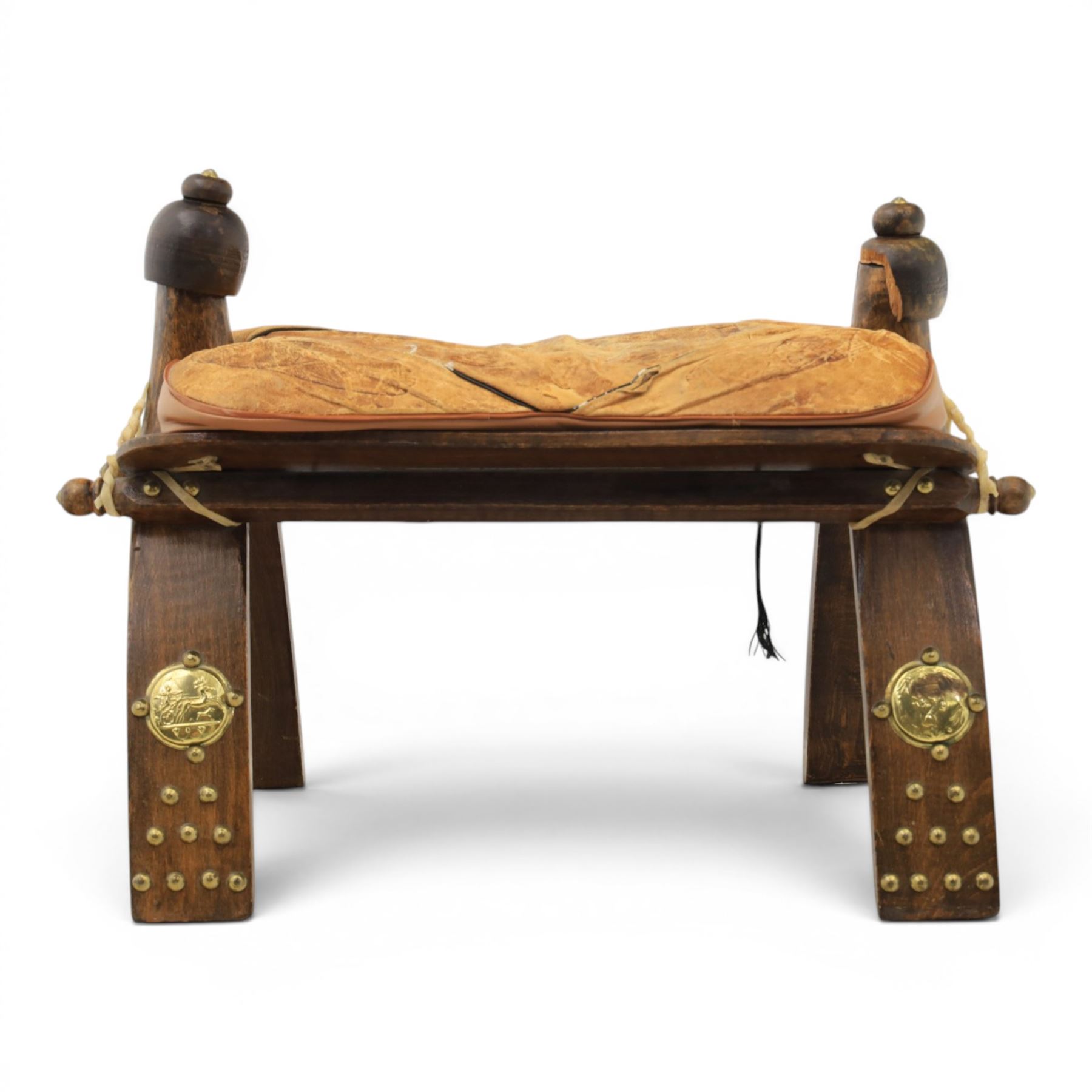 20th century Camel stool, with wooden turned finials, above a tooled leather seat, curved supports with brass applications 