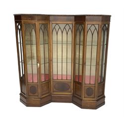 Early 20th century mahogany Gothic style display cabinet, faceted reverse break front, enclosed by three doors with pointed arch astragal glazing, on stepped and moulded plinth base