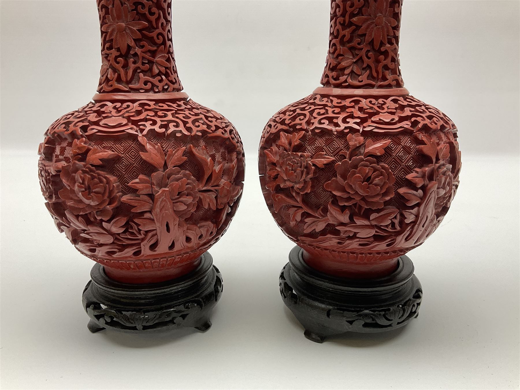 Pair of Chinese cinnabar lacquer vases, each of bulbous baluster form, carved with peonies and foo dogs amongst scrolls, with blue enamel interior and upon wooden bases, H20cm