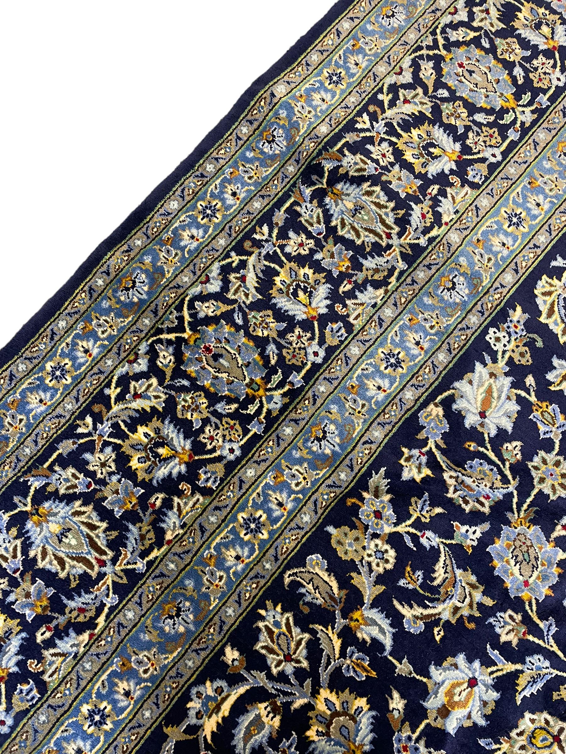 Central Persian Kashan indigo ground carpet, central lighter blue floral medallion surrounded by interlacing leafy branches and stylised plant motifs, the main border decorated with repeating floral motifs and scrolling branches, within guard stripes 