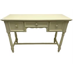 Cream finish side or dressing table, moulded rectangular top over three drawers, on turned supports united by H-shaped stretchers