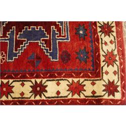 Caucasian Kazak hand-knotted rug, madder red ground with three large stepped geometric medallions in dark blue, ivory and red, surrounded by stylised star and flowerhead motifs, enclosed by ivory border with repeating eight-pointed stars, fringed ends