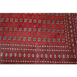 Large crimson ground Afghan Bokhara carpet, the field decorated with repeating Gul and geometric motifs, the multiple guard stripes with further geometric decoration