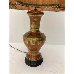 A large table lamp of baluster form, with scrolling gilt decoration upon a red ground, on circular ebonised base, together with a pleated fabric shade, lamp base H53cm. 