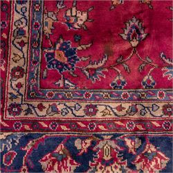 Large Persian-style mahal-type hand-knotted carpet, of rectangular form with a deep crimson field decorated with an all-over arrangement of stylized floral sprays and palmettes, with a central subtle medallion composition enclosed by a dark navy main border of scrolling floral motifs between narrow guard stripes with fringe ends 