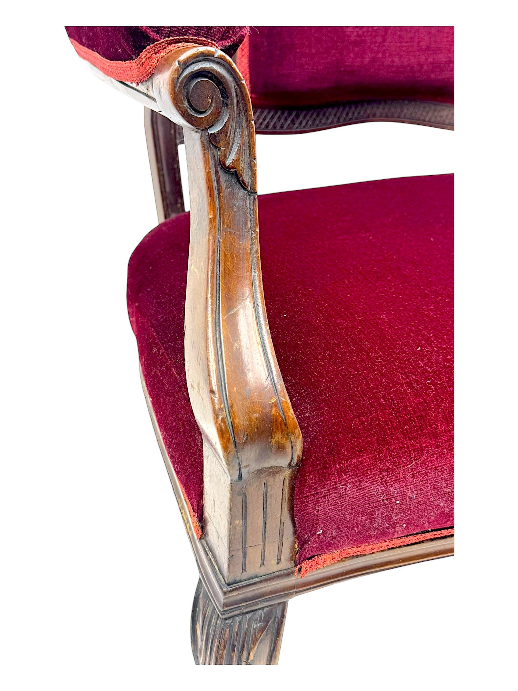 Late Victorian stained beech framed sofa, the backrests, seat and padded arms upholstered in deep red fabric, carved crest rail with scroll and foliate motifs supported by carved uprights, on cabriole supports with leaf carvings terminating in castors