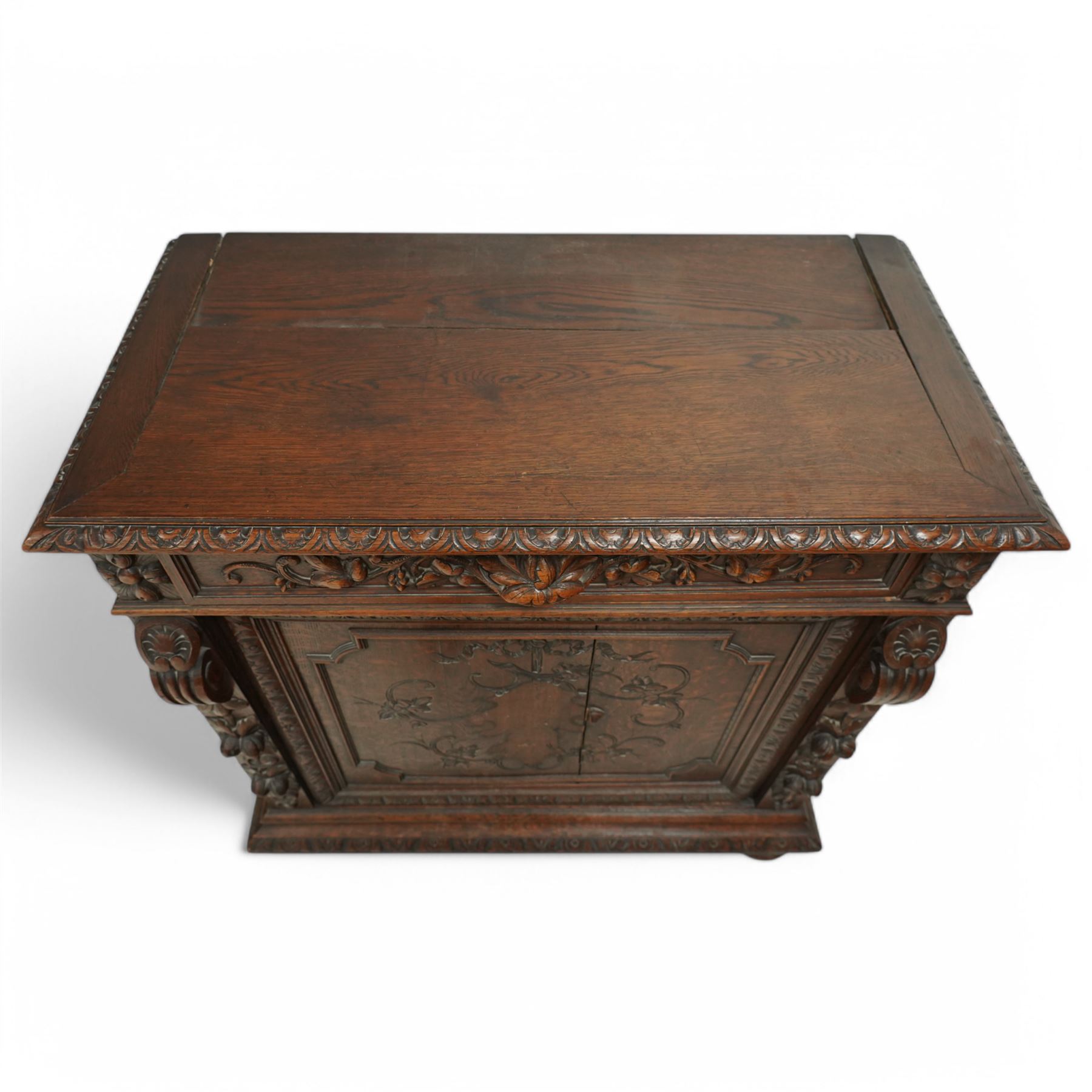 19th-century heavily carved oak baroque style cupboard with vine and floral carved frieze drawer above panelled cupboard door with floral carved appliqué (detached) flanked by symmetrically carved scroll and vine decorated sides, on bun feet 