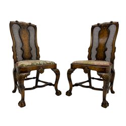 Pair of early 20th century Queen Anne design chairs, the cresting rail carved with scroll and central shell motif, shaped uprights and splat encased in cane work panels, shaped moulded seat frame with shell motif, floral needlework upholstered drop-in seat cushion, on shell carved cabriole supports with ball and claw feet, united by turned and shaped middle stretcher carved with acanthus leaf