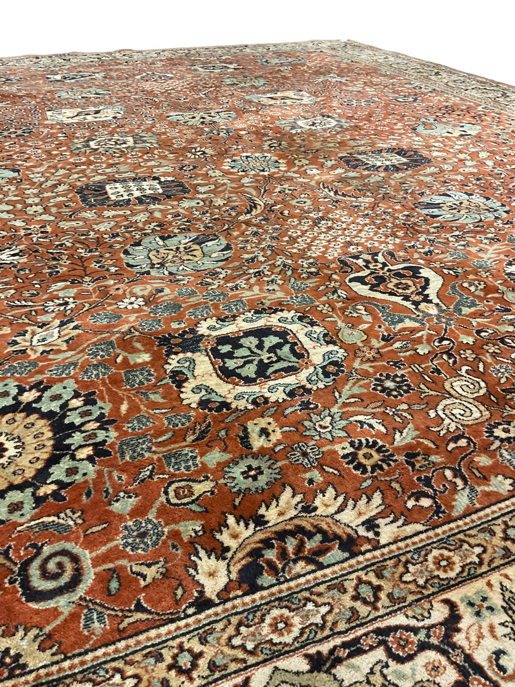 Persian design carpet, rust ground field decorated with large stylised plant motifs surrounded by smaller floral motifs, repeating trailing border