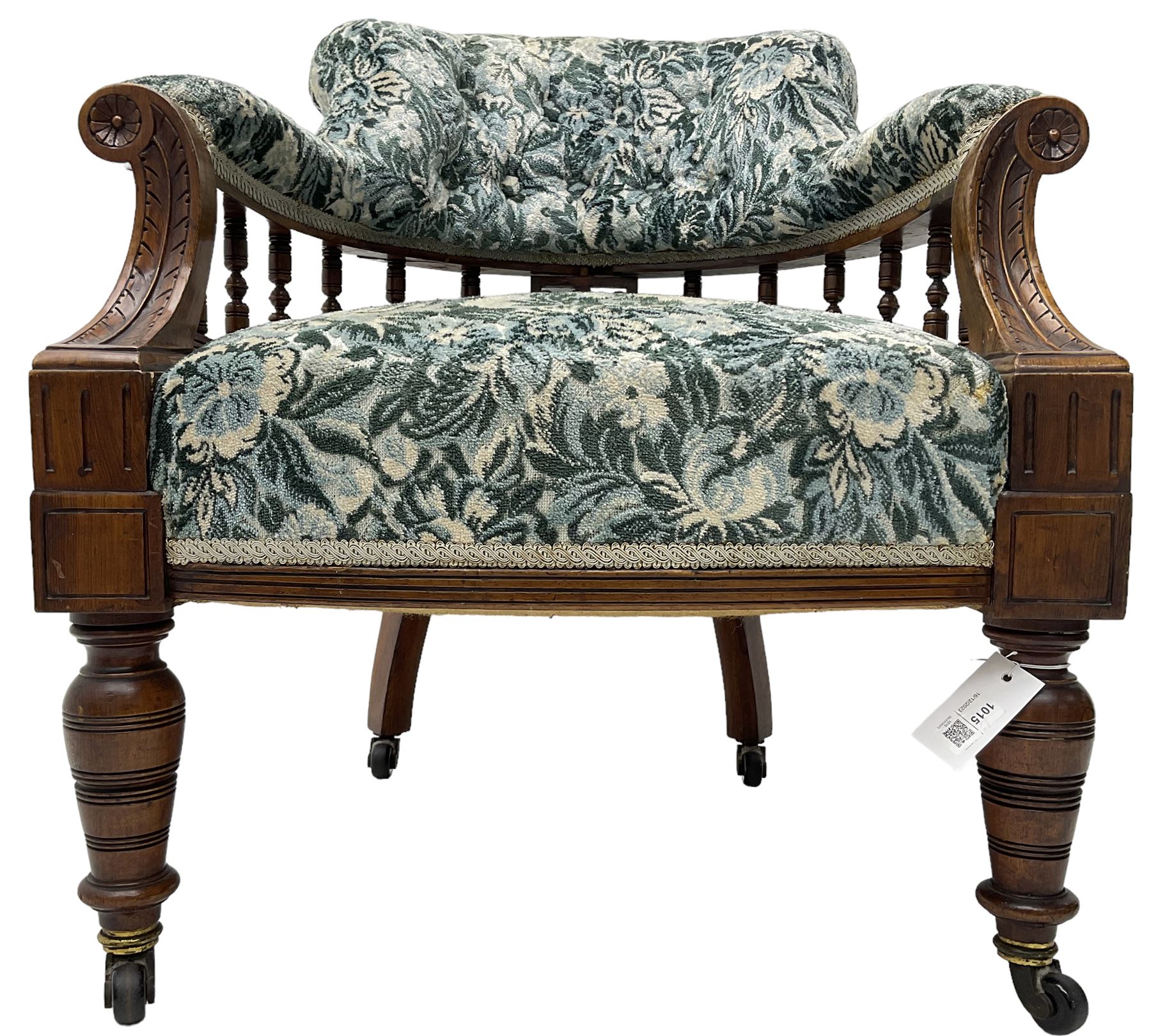 Victorian walnut framed tub-shaped armchair, the shaped rolled back supported by a spindle turned balustrade, upholstered in buttoned floral fabric, scrolled arms supports carved with acanthus leaves and flower heads, on collar turned feet with brass and ceramic castors
