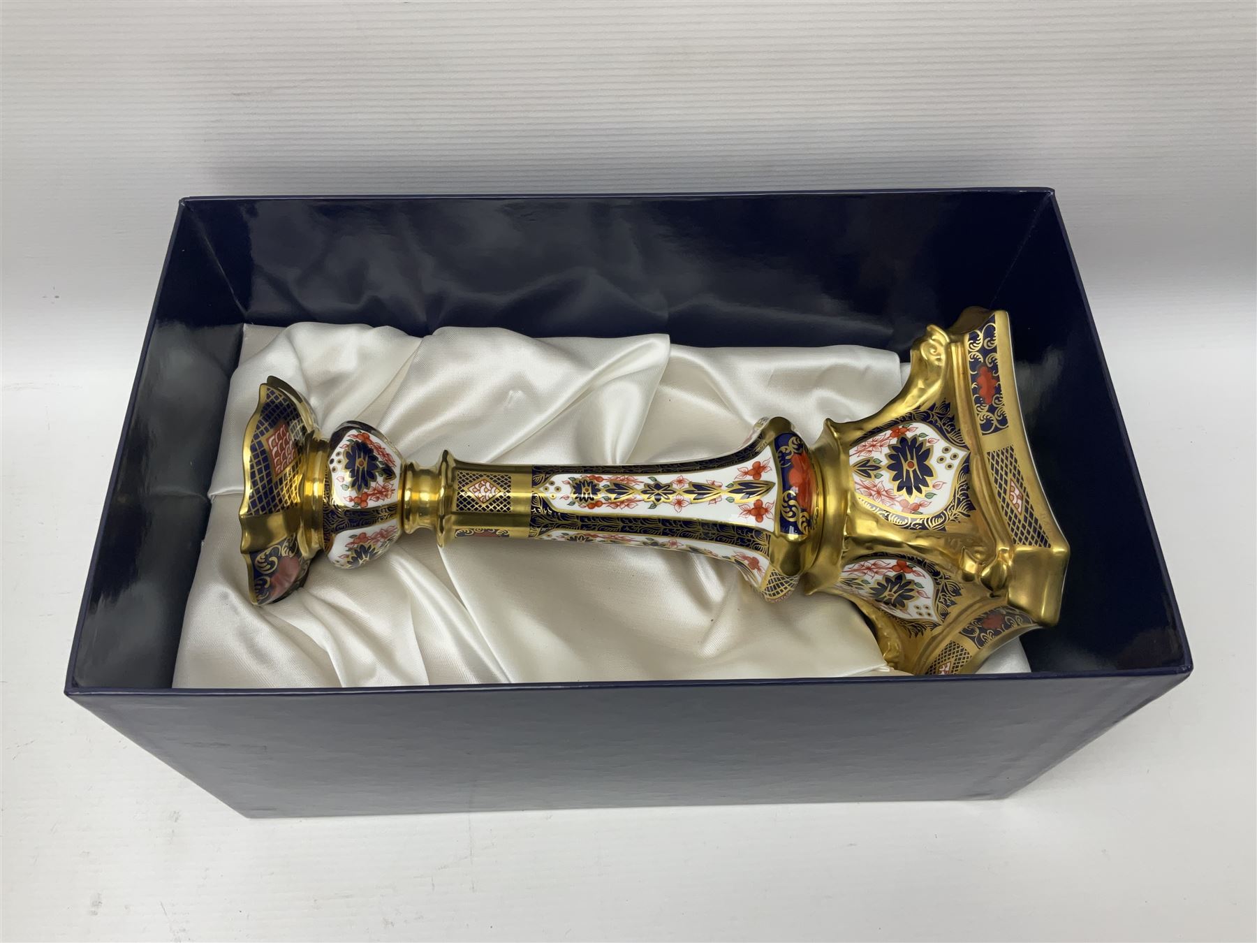 Pair of modern Royal Crown Derby Old Imari 1128 pattern candlesticks, each with shaped drip tray affixed to squat socket, upon spreading stem and canted square base with gilt dolphin edges, with printed marks beneath including Roman numeral year cypher for 2003, H26.5cm, with original boxes