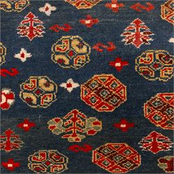 North East Persian Turkoman hand-knotted rug, deep teal blue field decorated with repeating rows of stylized octagonal guls and cruciform tribal motifs arranged in a lattice formation, enclosed composition featuring angular devices and reciprocal motifs, with cotton fringe ends