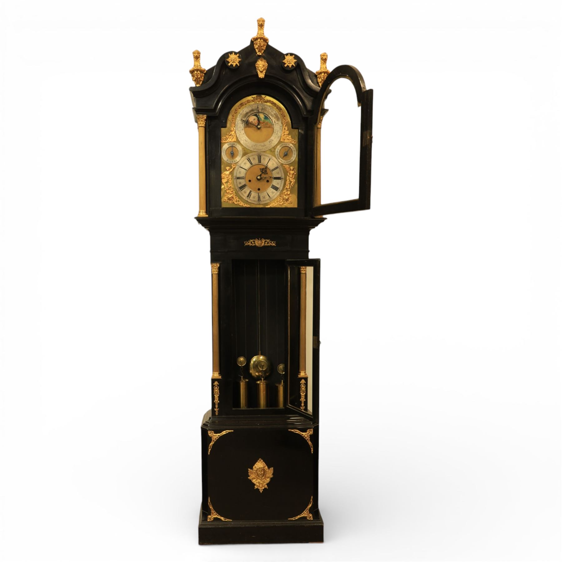 Late nineteenth century ebonised and gilt-bronze mounted musical longcase clock of impressive architectural form, the case of ebonised finish with applied gilt bronze neoclassical inspired masks and mounts, hood of arched form with glazed door, flanked by free fluted columns with gilt bronze Corinthian capitals surmounted by stylized Lion finials, frieze and arch enriched with applied foliate mounts, trunk with a rectangular glazed door bordered by mouldings and flanked by engaged columns with gilt bronze mounts above a shaped projecting base panel with applied central female mask and corner foliate ornamentation, arched brass dial, with a silvered chapter ring and applied cast gilt bronze spandrels and arch decoration, incorporating subsidiary selection dials for chime/silent and tune regulation, offering Cambridge chimes on eight bells and an additional chime sequence on ten bells, brass arch is further embellished with a moon phase aperture with lunar calendar scale, Zodiac symbols, month and date indication on a silvered dial, substantial eight-day, three-train movement with pinned cylinder musical train and a graduated nest of eleven bells with eleven hammers, quarter chiming with separate hour/half-hour strike and chime repetition, movement is regulated by an anchor escapement, with brass disc pendulum, three brass weights, two winding keys and case door key