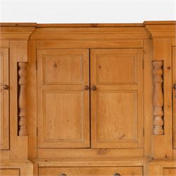Large Victorian stripped pine reverse breakfront housekeeper’s cupboard, the moulded cornice above a central pair of panelled cupboard doors flanked by single cupboard doors and divided by turned baluster pilasters, the lower section fitted with an arrangement of twelve drawers with knob handles, raised upon bun feet