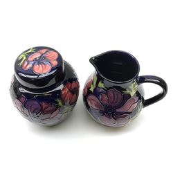 A Moorcroft jug decorated in the Anemone pattern upon a dark blue ground, with impressed and painted marks beneath, H14.5cm, together with a similarly decorated Moorcroft ginger jar and cover, with impressed and painted marks beneath, H15.5cm. (2). 