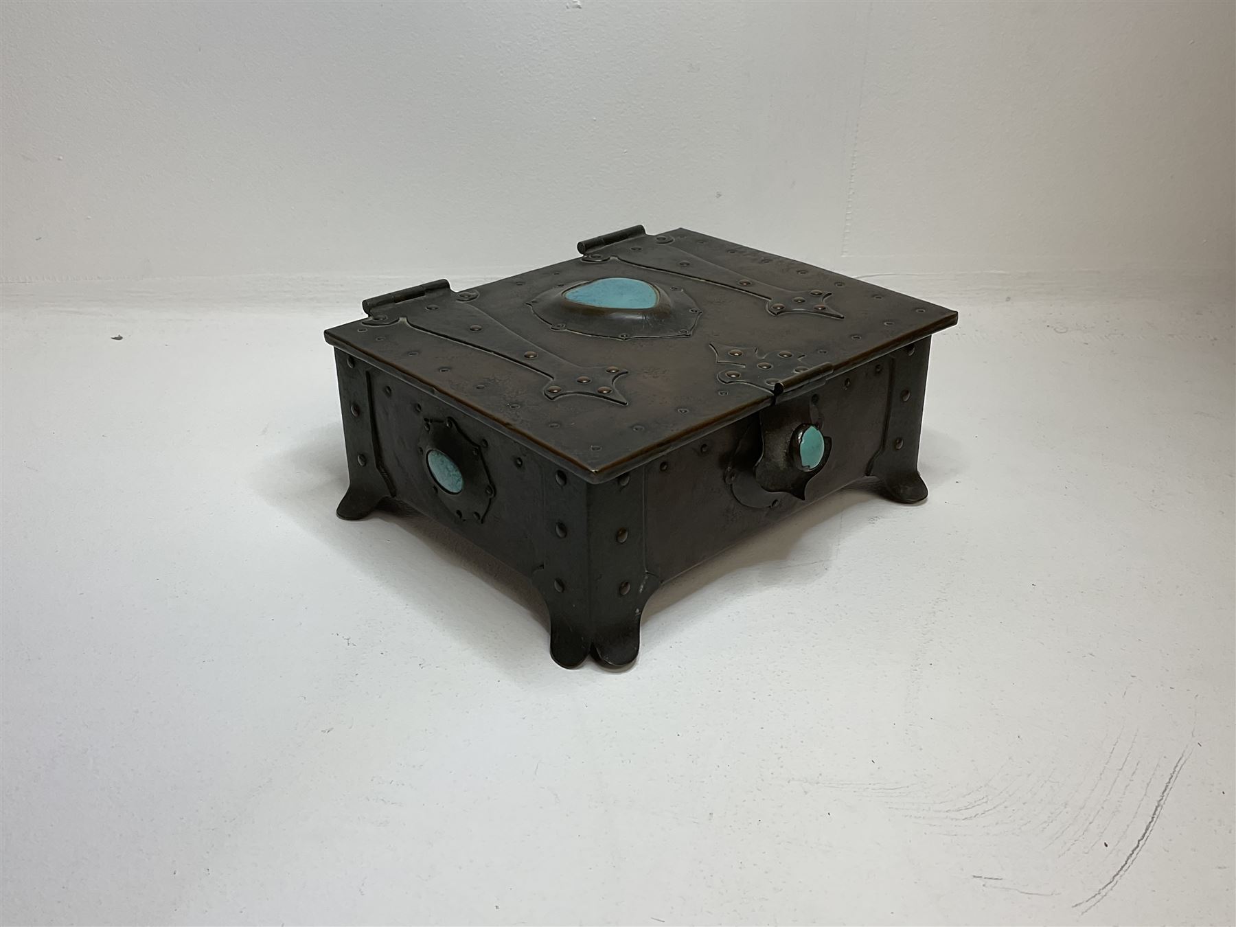 Arts and Crafts copper box, the lid decorated with stylised riveted hinges and inset with Ruskin type ceramic turquoise heart-shaped cabochon, the mount etched M.B 1913, and further cabochon roundel to each side panel, including one inset to the clasp acting as the knob to the locking mechanism, marked RS Douglas 1913 beneath, W16.5cm H7cm D15cm