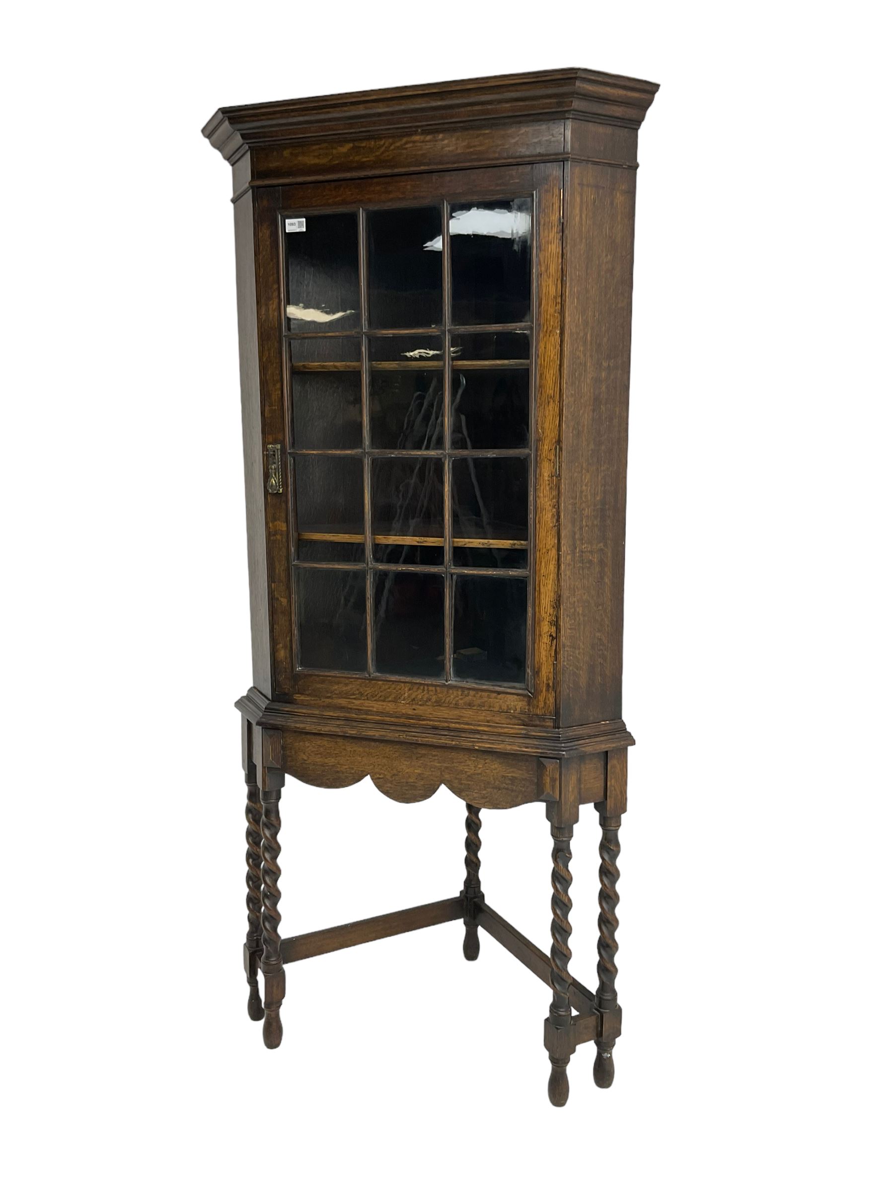 Early to mid-20th century oak corner display cabinet, projecting cornice over astragal glazed door, on spiral turned supports joined by stretchers