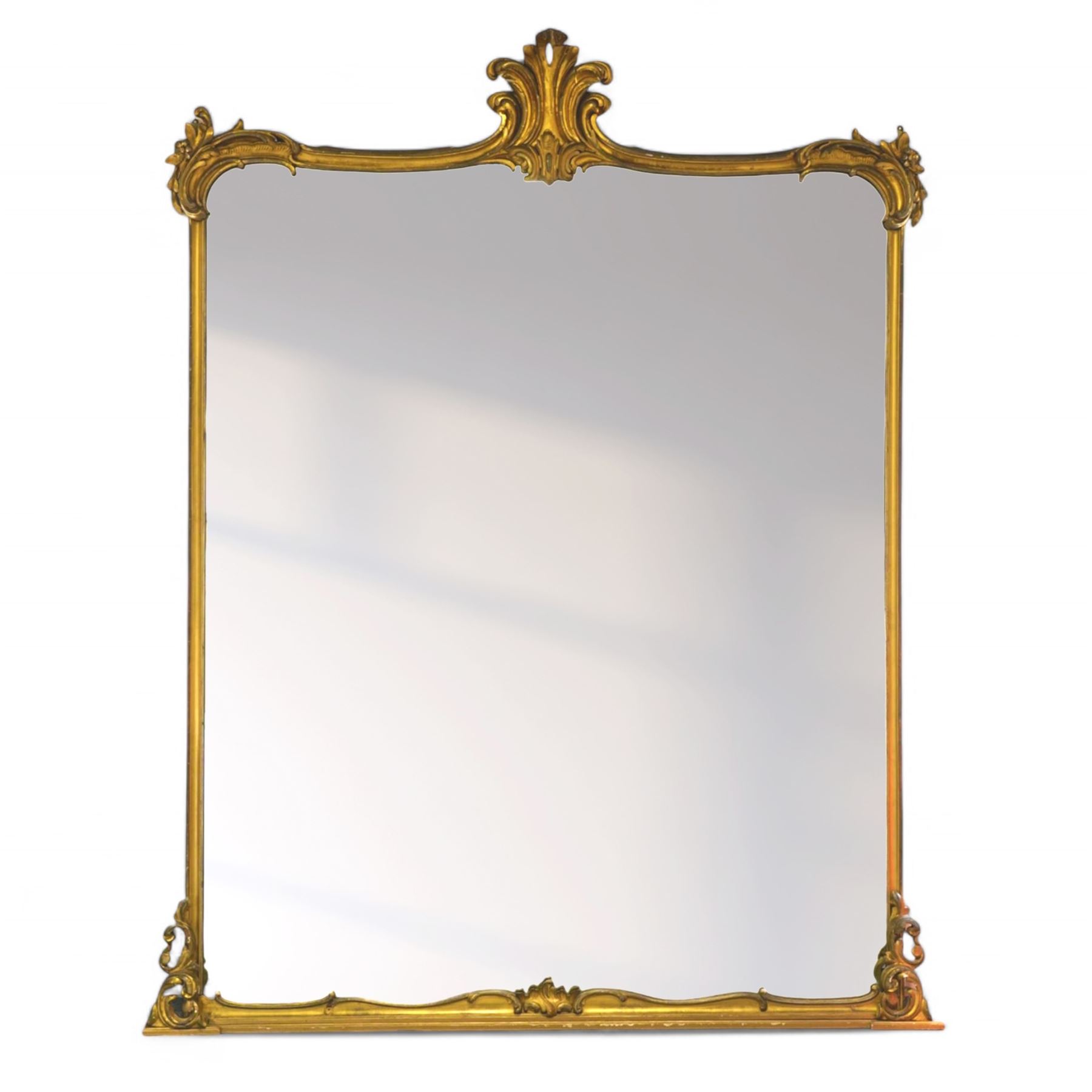 Large Victorian gilt wood overmantle mirror, shaped cresting rail with curled acanthus leaf pediment, the corners decorated with foliate C-scrolls and flower heads, curled foliage lower corner brackets, plain mirror plate 