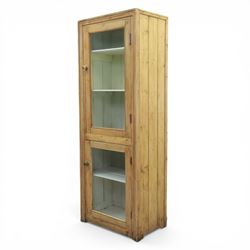 Early 20th century waxed pine kitchen cupboard, rectangular form with moulded top, enclosed by two glazed doors revealing painted interior with shelves, boarded sides and back, fitted with brass knob handles