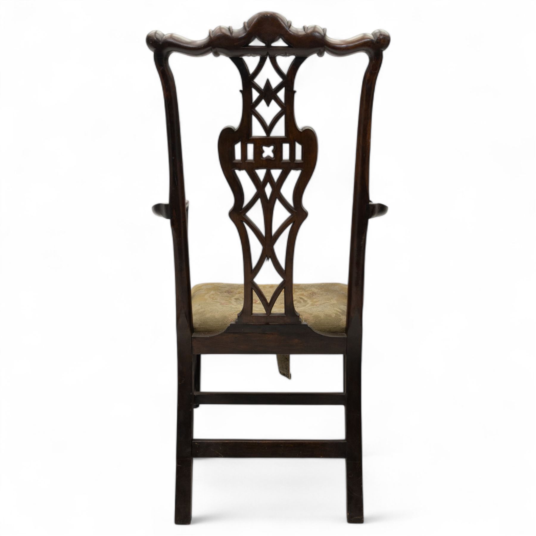 19th-century Chippendale Revival design mahogany oversized high-back armchair, serpentine crest carved top rail above pierced back splat with interlaced ribbon carving and geometric fretwork design, and outward scrolling arms above drop-in needlework seat on square chamfered legs 