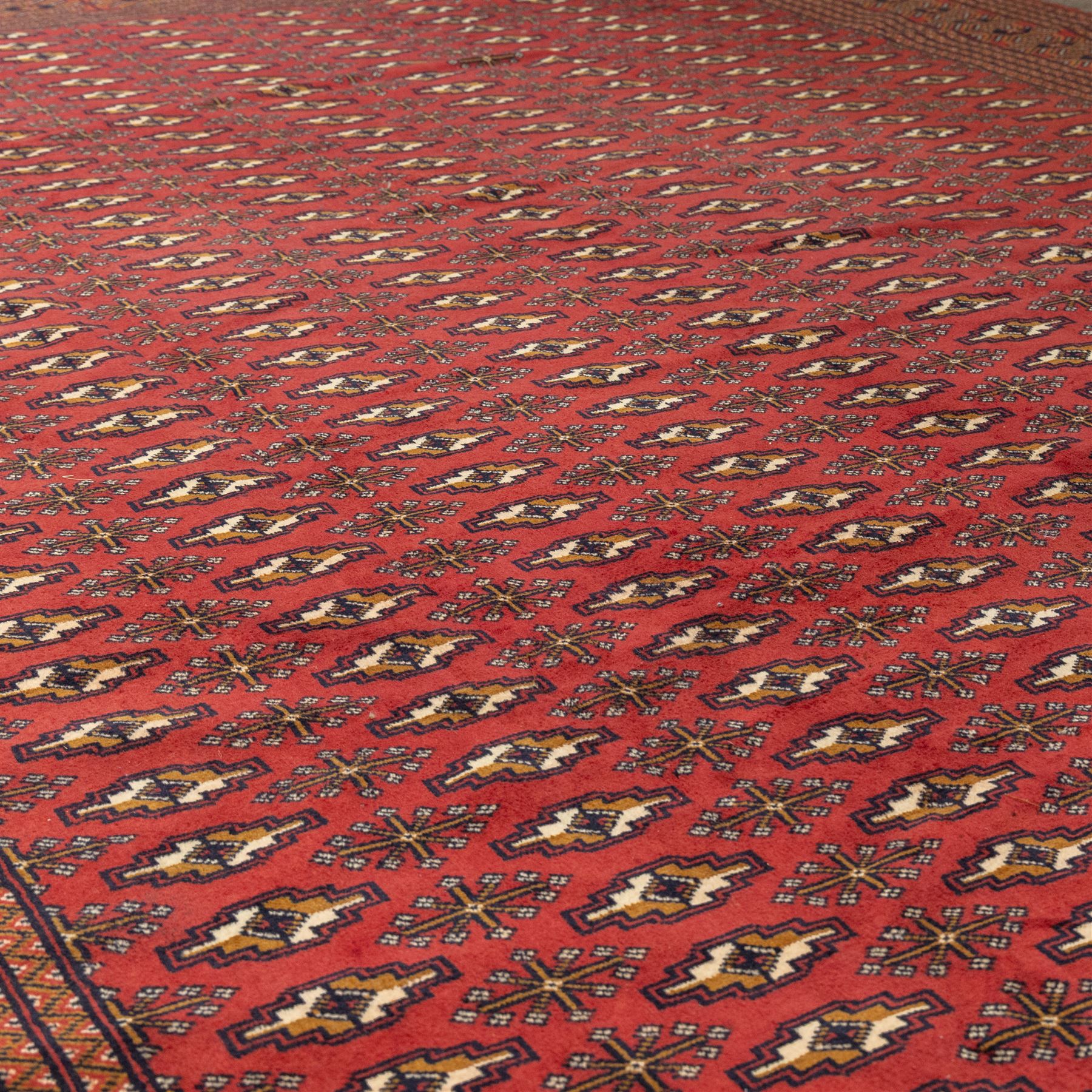 North East Persian Turkoman hand-knotted carpet, madder red field decorated with rows of repeating Tekke guls, in offset horizontal bands and interspersed cruciform subsidiary motifs, enclosed within narrow geometric borders featuring stylized tribal devices, with fringe ends   