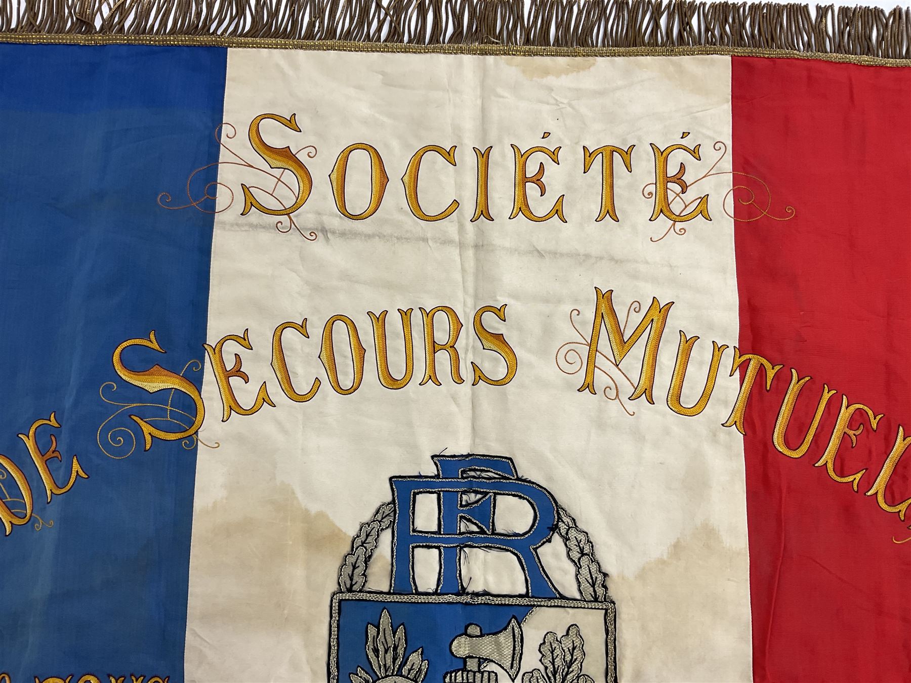 French State Police banner as the tricolor flag embroidered with coloured and metallic thread 'Societe De Secours Mutuels Un Pour Tous Tous Pour Un De La Police D'Eteat De Marseille' to one side; plain flag verso; tassels to three sides 100 x 113cm