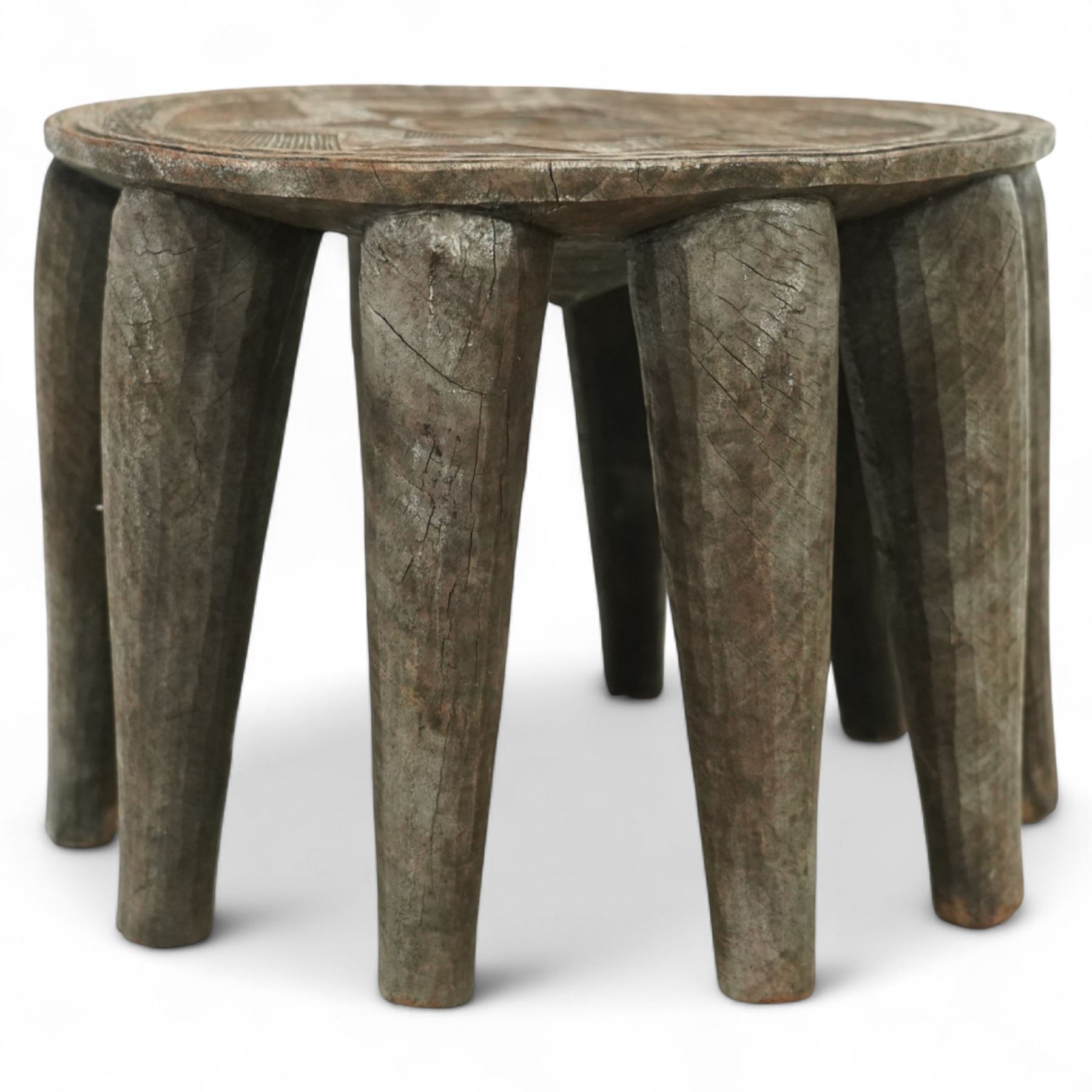African Nupe carved tribal stool, the rounded top with repeating incised decoration and rope-edge border, supported by ten tapered legs D37cm