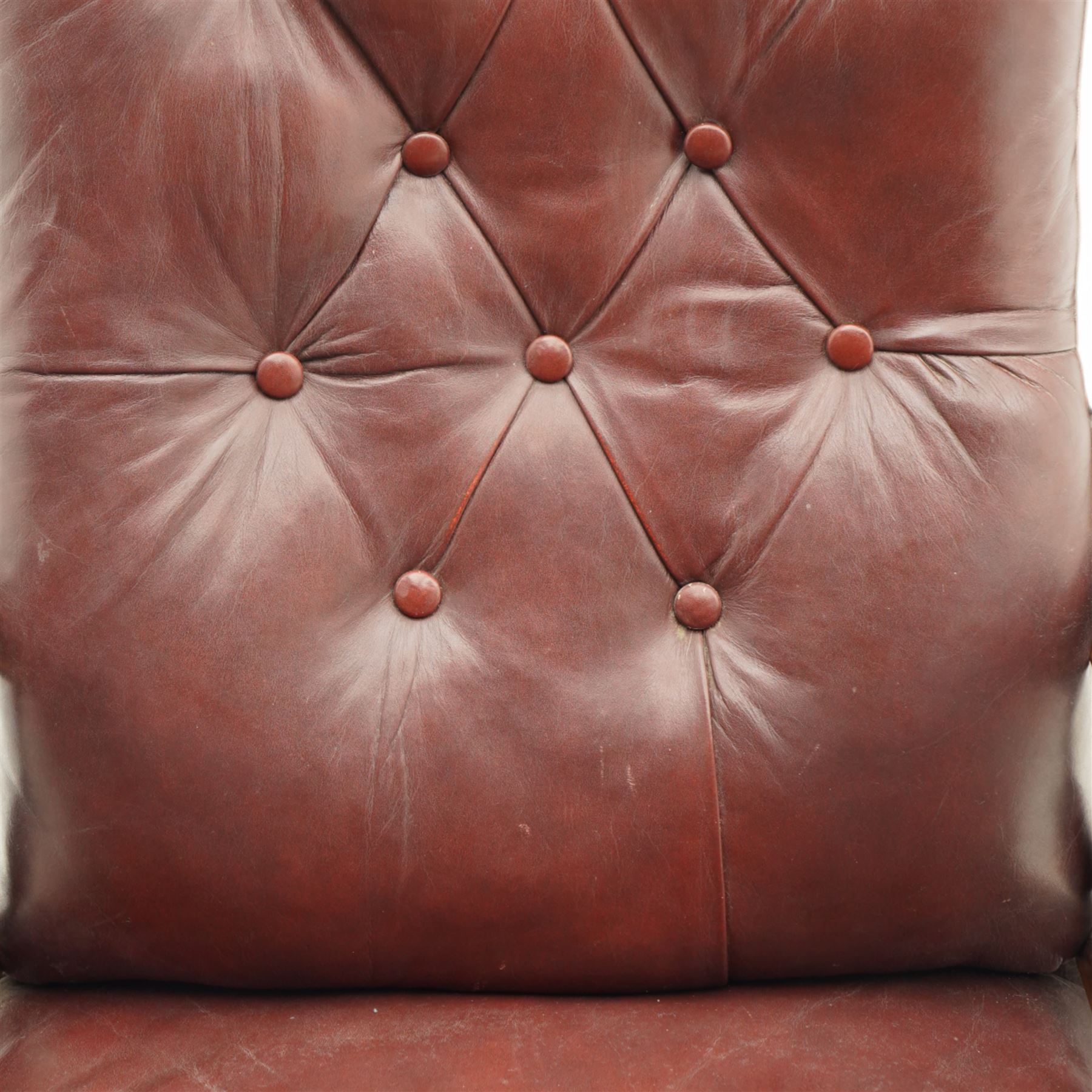 Late Victorian mahogany open armchair, arched cresting rail decorated with turned roundel, upholstered in buttoned burgundy leather, the upholstered arms on turned and lobe carved balustrade, turned and lobe carved front feet with brass and ceramic castors 