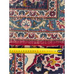 Pair of Persian wool rugs, each with rich red ground, one centred with a diamond-shaped medallion and navy spandrels within a floral field, the other with radiating floral medallion and scrolling foliate motifs, both enclosed by multiple borders with palmette and flowerhead designs, from the region of Kashan 291x376, 299 x 378 