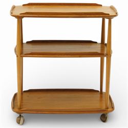 Ercol - elm tea trolley, Model 458. Rectangular three-tier form with shaped gallery edges, supported on turned upright supports, raised on castors