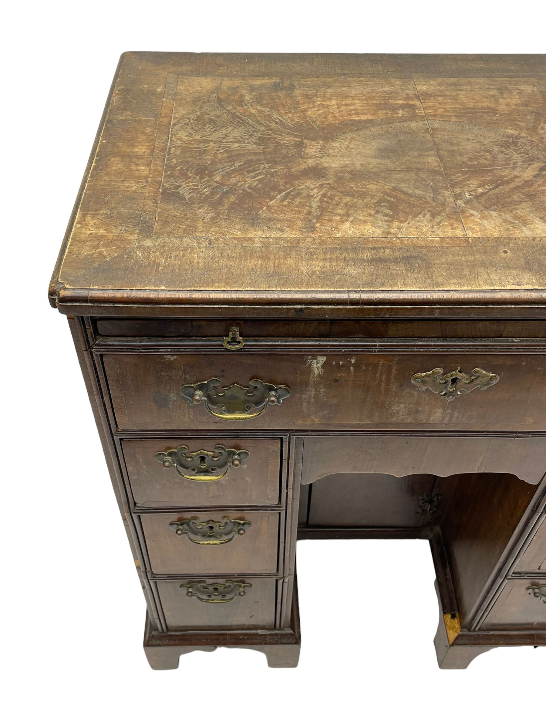 Georgian walnut kneehole desk, moulded rectangular top with book-matched veneers within crossbanding, fitted with slide over one long drawer, frieze drawer, six small drawers and recessed cupboard, raised on bracket feet