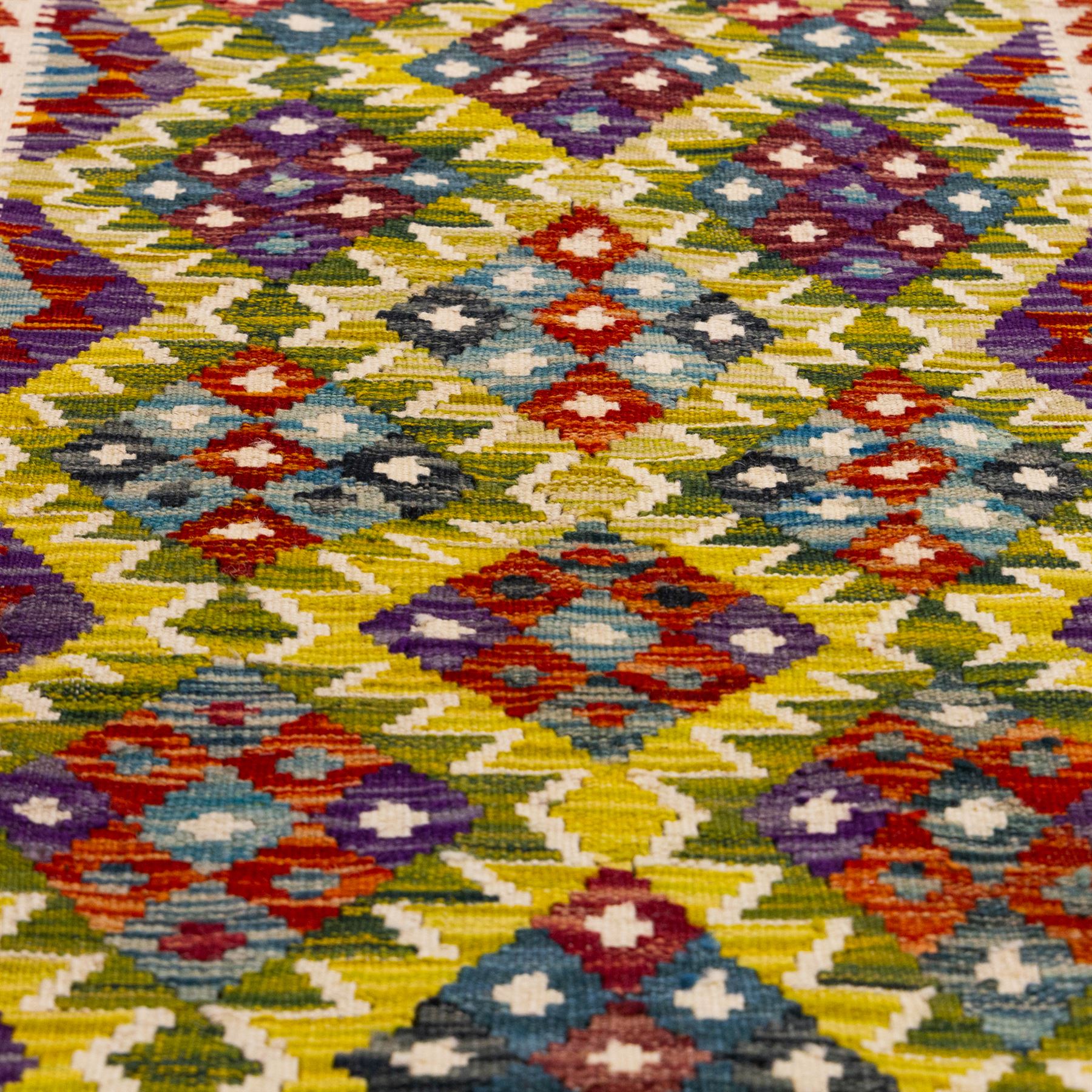 Afghan Maimana kilim flatweave runner, central field features large bold nested diamond motifs and stylized geometric lozenge patterns on olive purple, blue, and green tone ground, border stripe in teal ground, and fringe