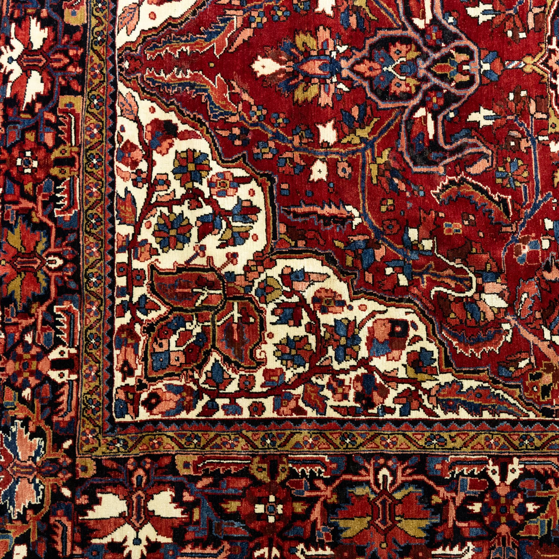 North West Persian Ahar hand-knotted carpet, madder red ground, with a large central shaped floral medallion with pendants, surrounded by angular scrolling foliate motifs incorporating rosettes, palmettes and stylised flowerheads, enclosed by ivory spandrels and a dark navy border with repeating geometric floral motifs and meandering vines, flanked by narrow patterned guard stripes, with cotton fringes