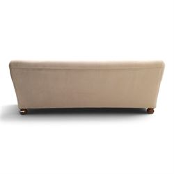 Late Victorian oak framed low three-seat settee, of traditional shape with low rolled sprung back over rolled arms and sprung seat, raised on front turned feet, upholstered in beige fabric