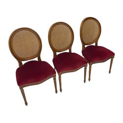 Set six French style walnut finish dining chairs, oval cane bergere backs over serpentine seats upholstered in red, flower head carved fluted supports