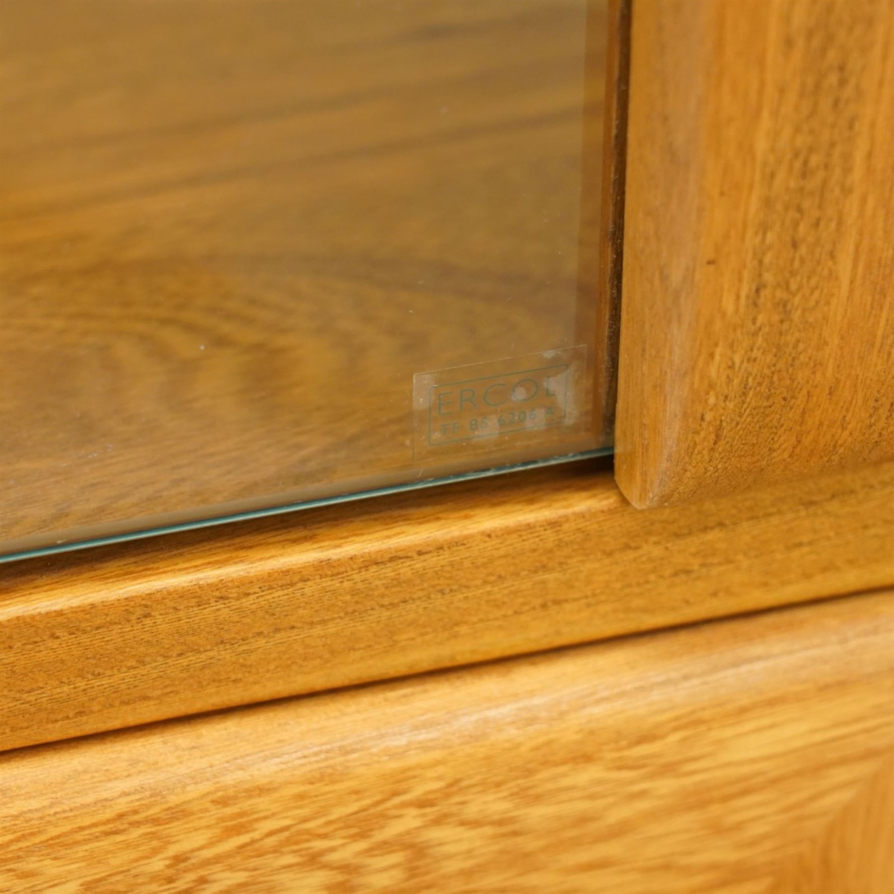 Ercol - elm corner display cabinet, Model 3856. Glazed upper section with glass door enclosing two glass shelves and interior light, above panel cupboard door, with rounded uprights and circular turned handles, on plinth base