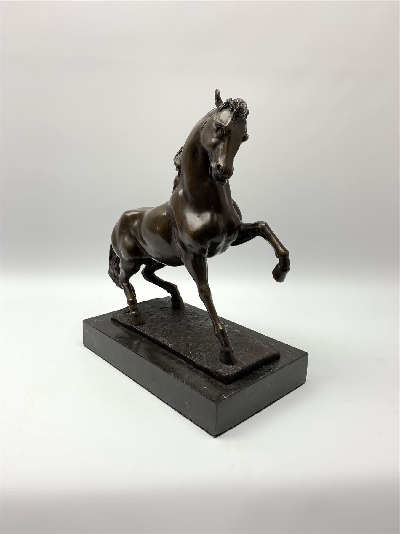 Bronze figure modelled as a prancing horse, upon a naturalistically modelled rectangular base, and black marble plinth, H34.5cm, L31cm