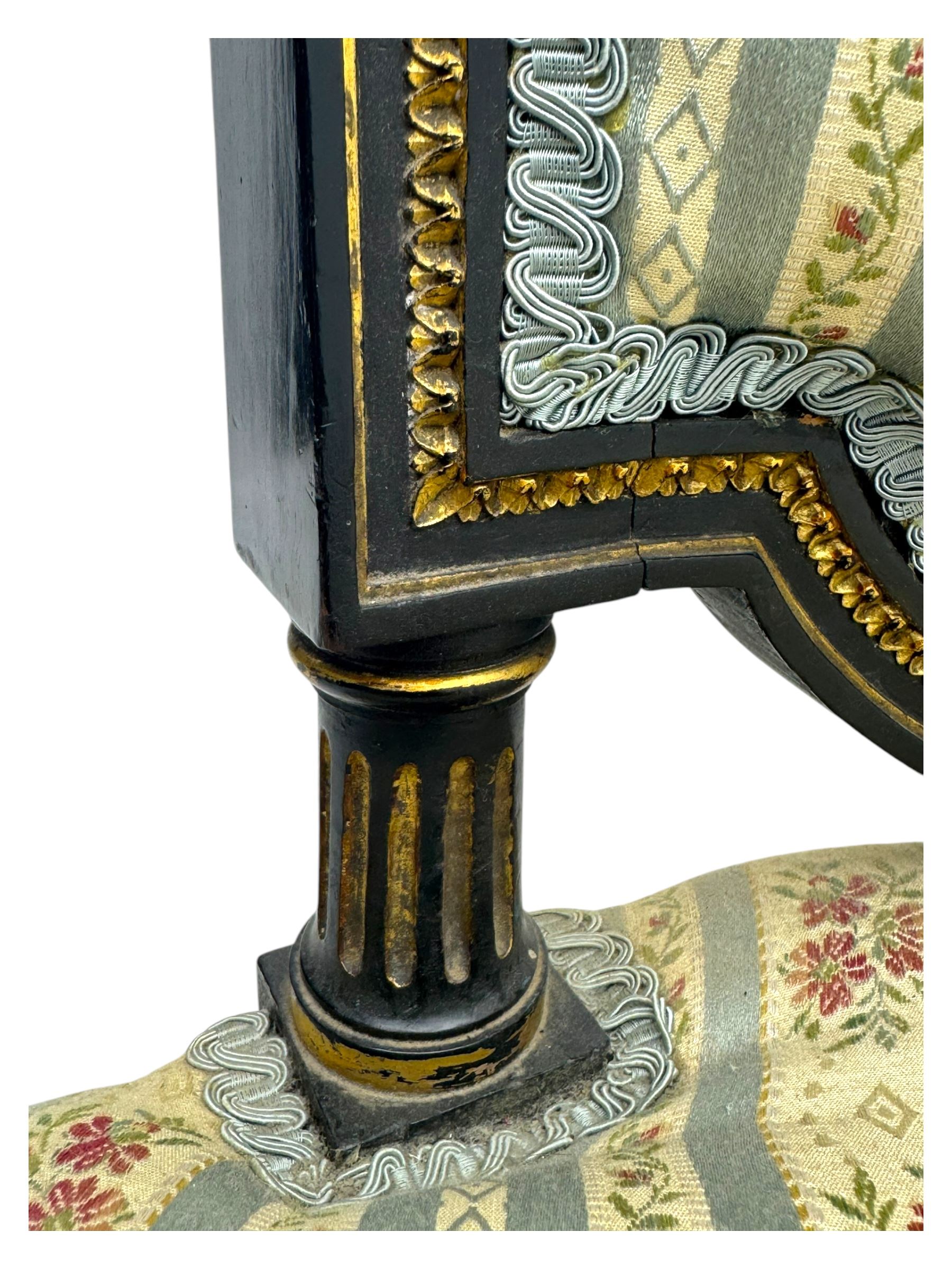 19th century French ebonised low chair, upholstered in floral striped fabric within a moulded frame with gilt line and foliate decoration, the seat of serpentine form, raised on turned fluted legs with toupie feet