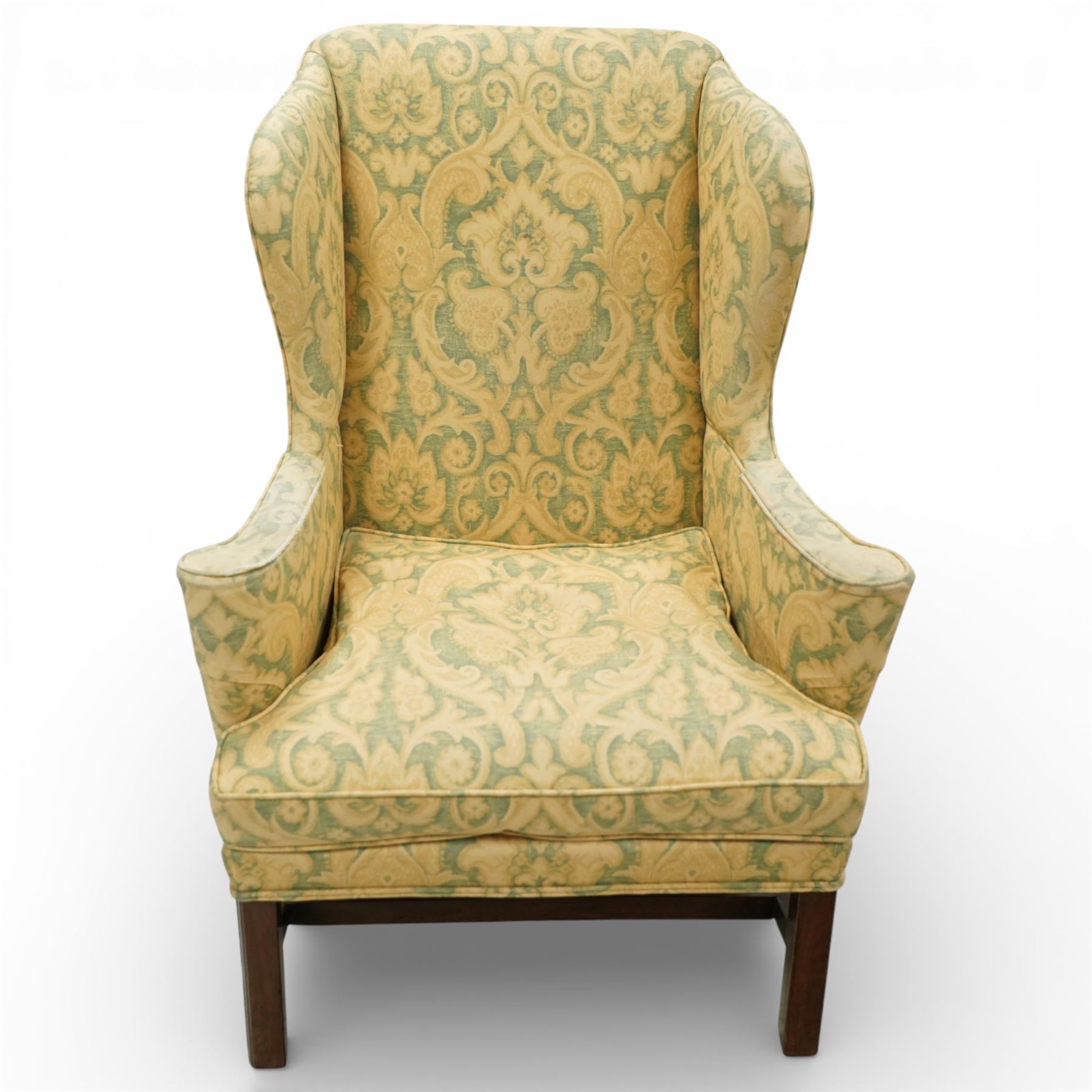 George III wing back armchair, the tall upholstered back with deep wings and gently shaped outline, padded arms flowing into the seat, loose cushion seat upholstered in a foliate patterned fabric, standing on square legs joined by stretchers