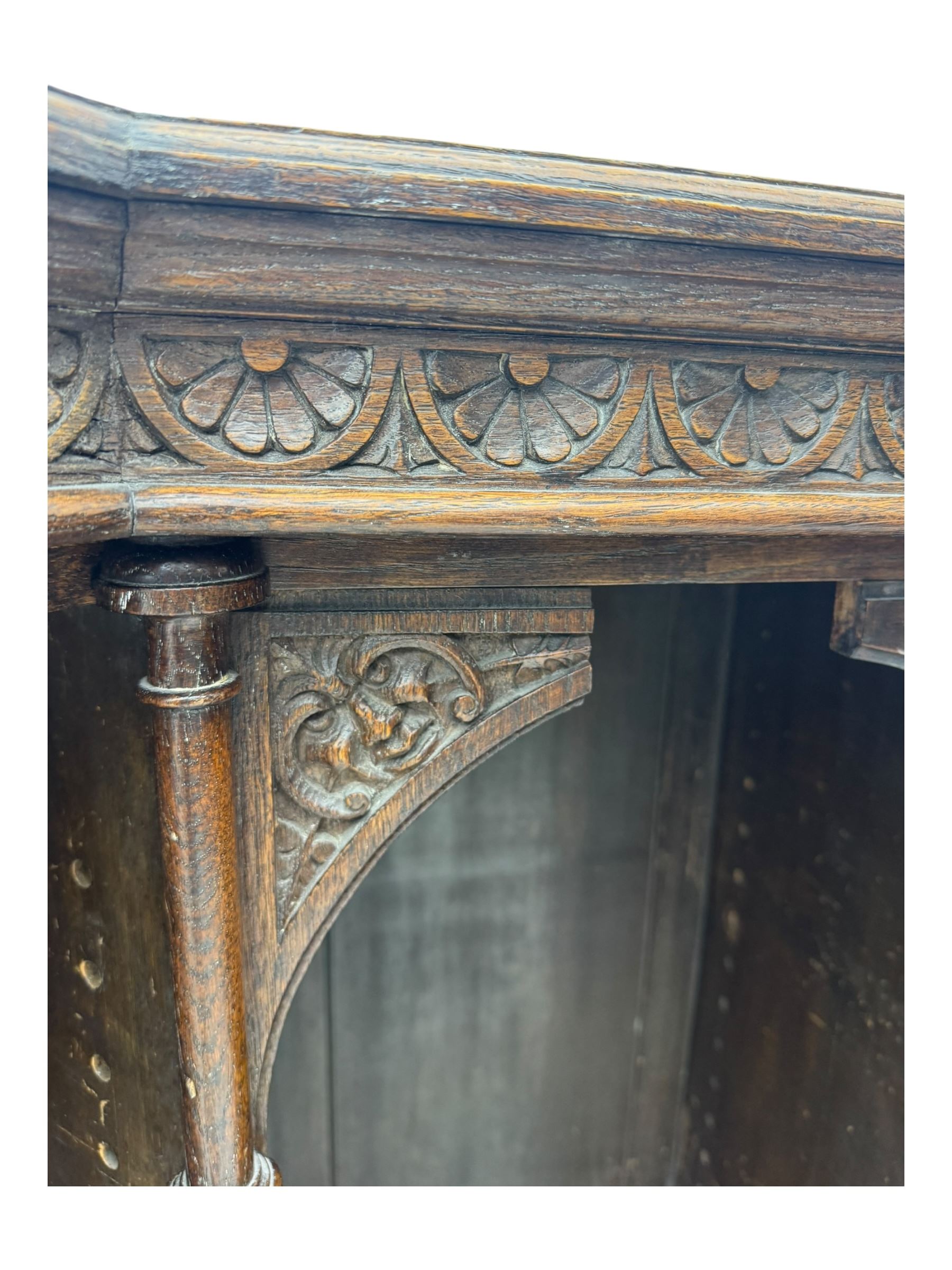Victorian carved oak corner bookcase, L-shaped form, moulded top over lunette carved frieze, decorated with S-scroll and mask carved corbels with trailing acanthus leaves, fitted with adjustable shelves, on moulded plinth base 