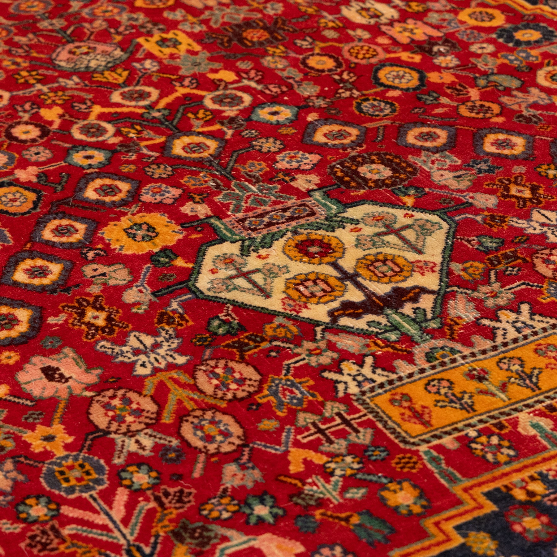 North Persian crimson ground rug, the field densely decorated with stylised flowering plants, urns and polychrome rosettes, within a stepped ochre outline, dark ground floral spandrels and geometric side panels
