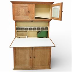 Early 20th century 'Quicksey' oak kitchen larder, rectangular moulded cornice over a pair of panelled cupboard doors, the fall front enclosing a white enamel work surface with fitted interior comprising original glass drawers, storage compartments and shelf, the lower section with twin panelled cupboard doors enclosing shelving and divided storage, raised on a plinth base