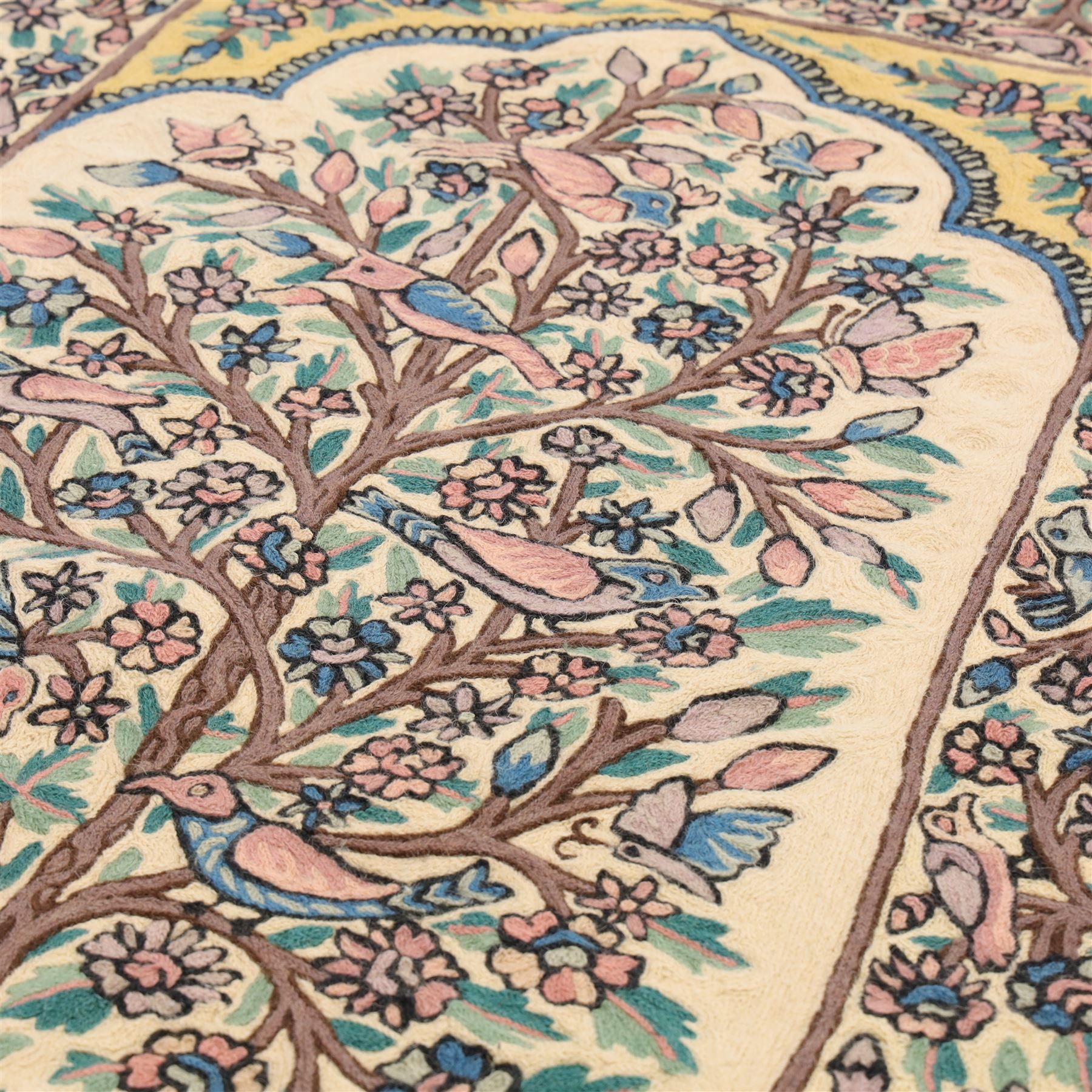Kashmiri chain stitch crewel embroidered wall hanging, the tree of life design embroidered on a cream ground with coloured pastel tones of rose, teal blue, and light brown in an arched mihrab style framing 