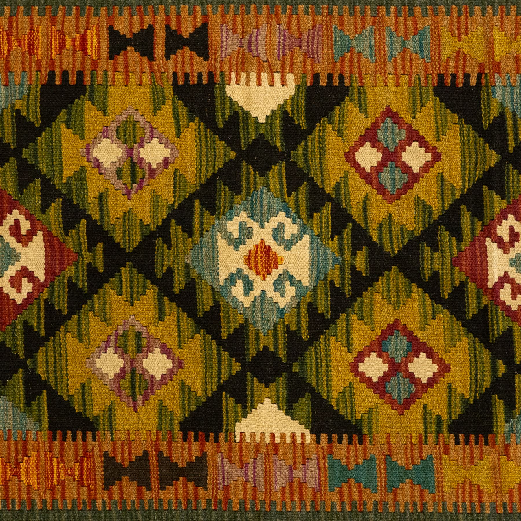 Chobi flatweave kilim runner with a repeating stepped diamond medallion design in live green, rust, teal, purple, and ivory, framed by chevron and geometric borders
