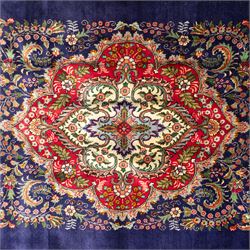 Persian Kashan rug, deep blue ground with central red and ivory lobed medallion framed by dense floral motifs, multiple borders with foliate and geometric design in red, blue and ivory, from the central Iran region