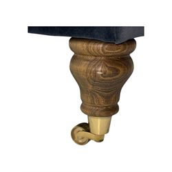 Contemporary square footstool upholstered in navy armour smart velvet, featuring a deep padded top, turned wood supports, and brass castors