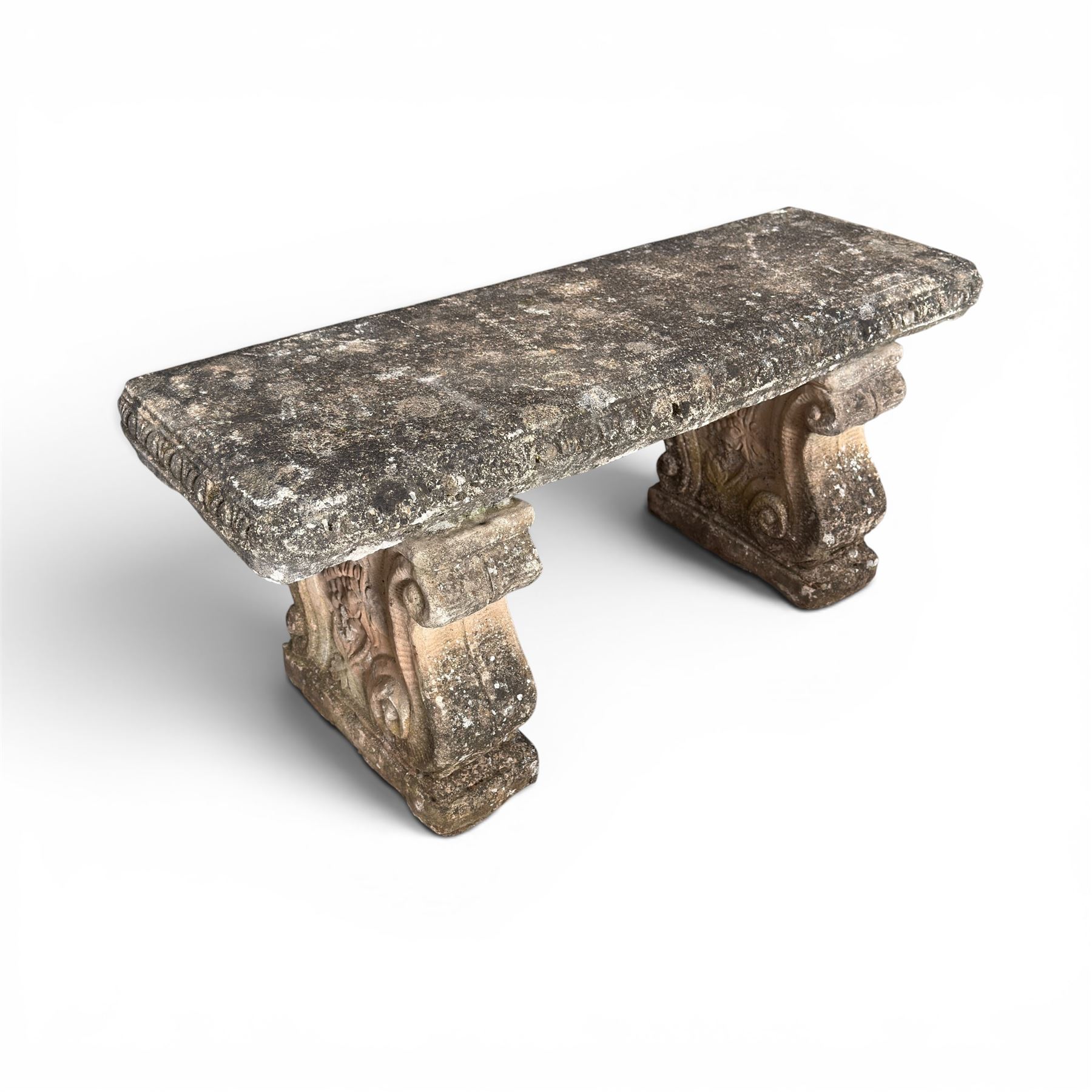 Weathered cast stone three-piece garden bench, with rectangular seat with egg-and-dart moulded edge, raised on end supports decorated with S-scrolls and fruiting vines